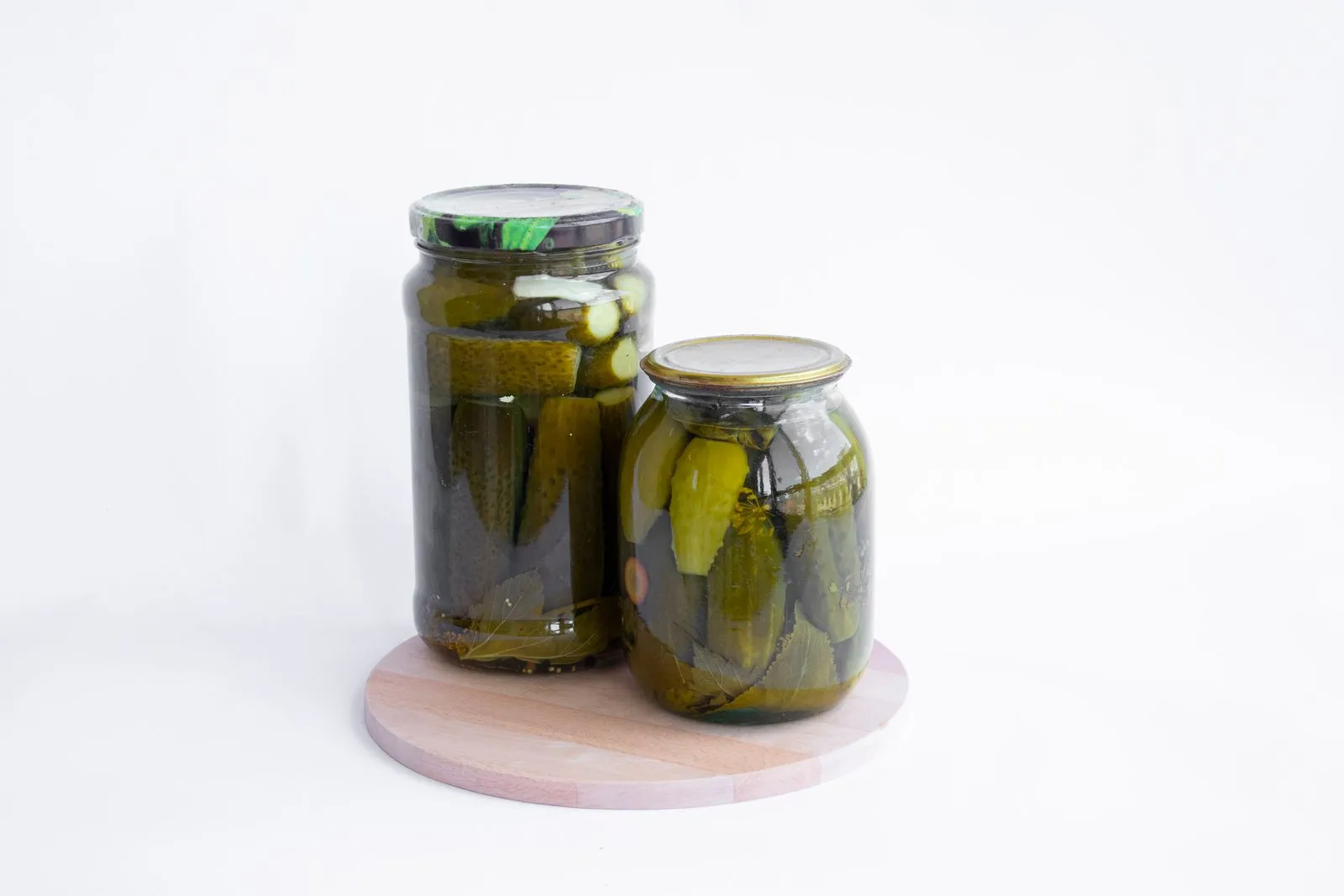 Two jars of pickles sit on a wooden board, showcasing preserved cucumbers in a still life composition.